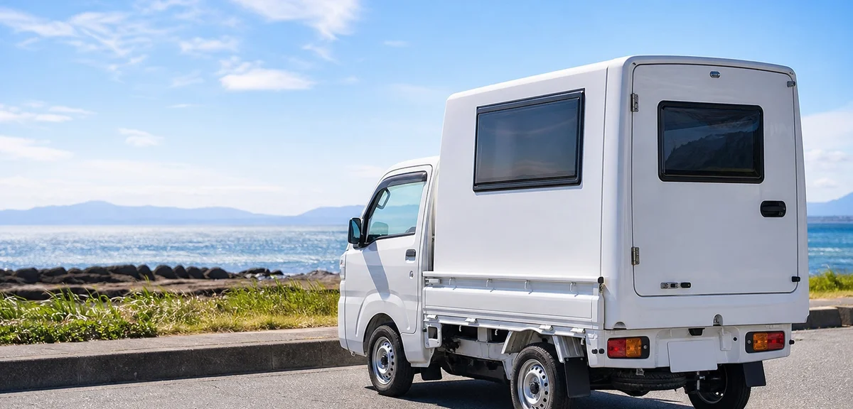 軽トラックの荷台に載せられた白いキャンピングシェル、海沿いの駐車場、晴れた日、写実的、文字なし