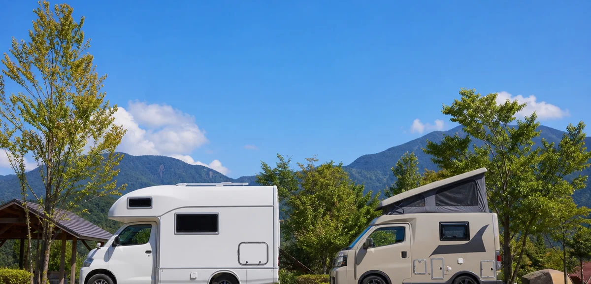 2台のコンパクトな商用バンベースのキャンピングカーが並んで停まるオートキャンプ場、横から見たサイズ感の比較、晴れた日、写実的、文字なし