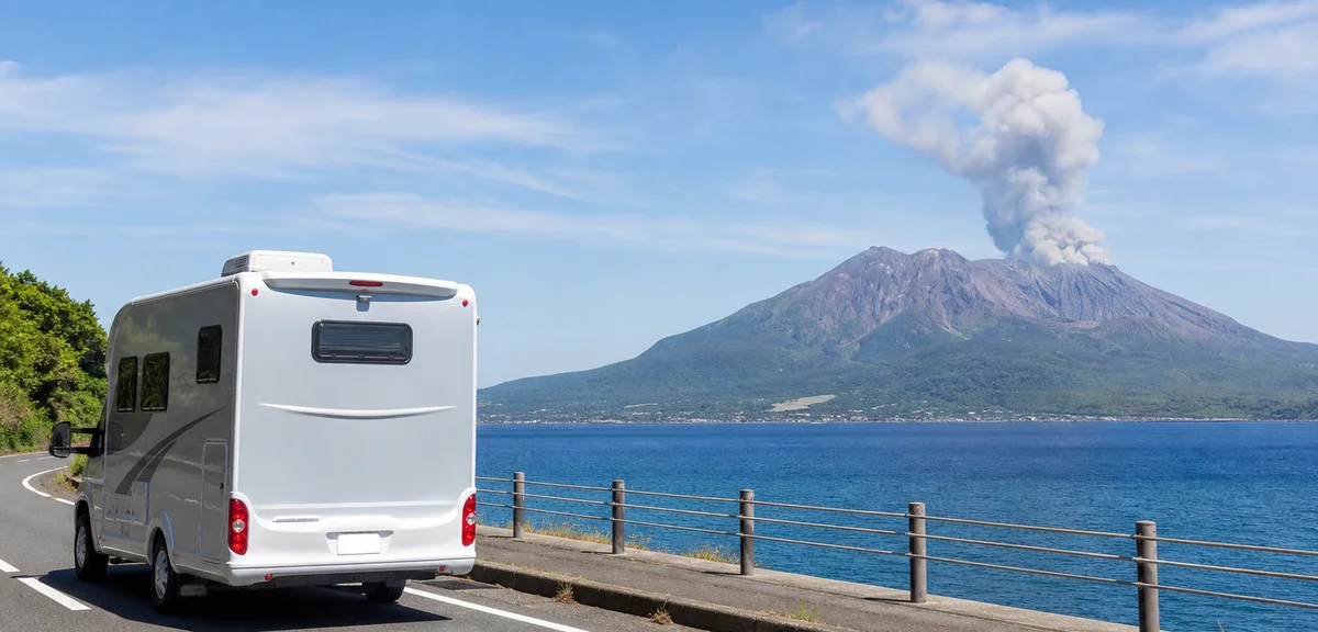 錦江湾沿いの道路を走るキャンピングカー、対岸に噴煙を上げる桜島、青い海と空、写実的、文字なし